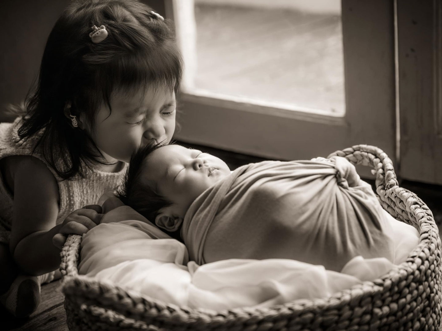 Newborn photoshoot of a little girl kissing her newborn sister in natural light photo studio at White Room Studio, 219 River Valley Road Singapore