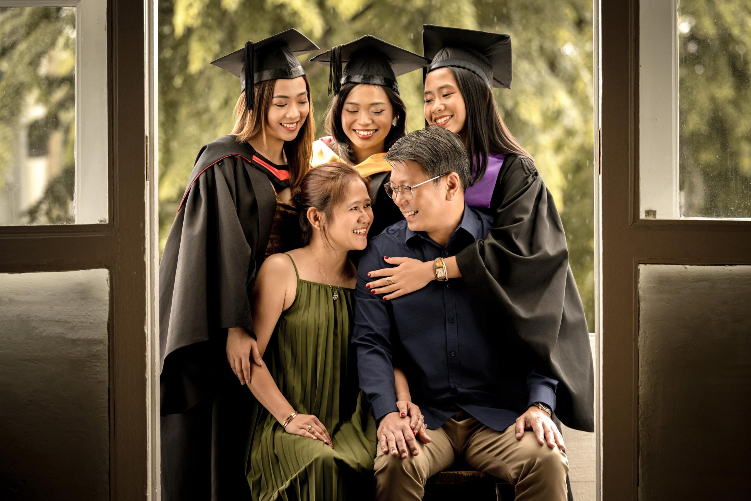 Graduation photoshoot of three daughters in gown and cap with parents in natural light photo studio at White Room Studio, 219 River Valley Road Singapore